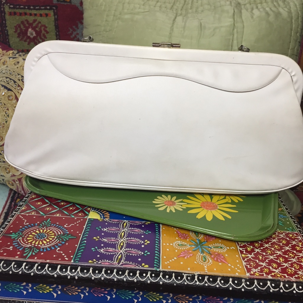 White structured baguette bag with a curved flap, photographed on a patterned green fabric background
